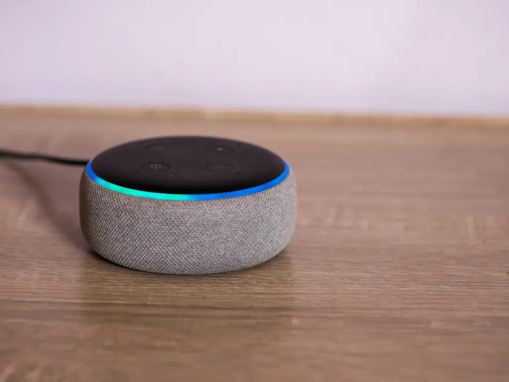 Compact smart speaker acting as a smart home hub, sitting on a wooden table with an illuminated LED ring.
